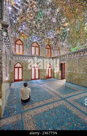 A man prays in the Ali Ibn Hamzeh Holy Shrine elaborately decorated inside with shiny mirror tiles (aina-kari). Shiraz, Iran. Stock Photo