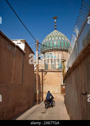 A man on motorbike ride in a narrow street towards the 19th century Nasir al-Mulk Mosque, aka the Pink Mosque. Shiraz, Iran. Stock Photo