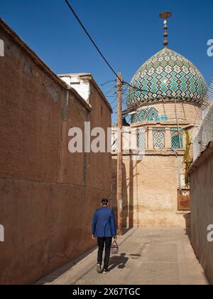 A man walks in a narrow street towards the 19th century Nasir al-Mulk Mosque, aka the Pink Mosque. Shiraz, Iran. Stock Photo