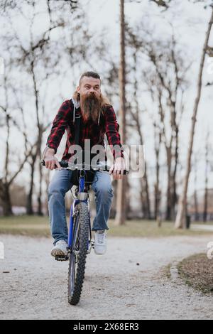 Active bearded man riding a bicycle in a park with trees in the background Stock Photo