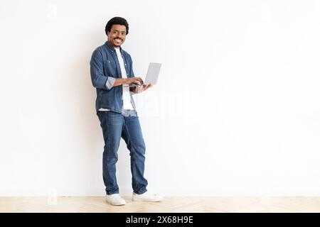 Man Standing in Front of White Wall Holding Laptop Computer Stock Photo