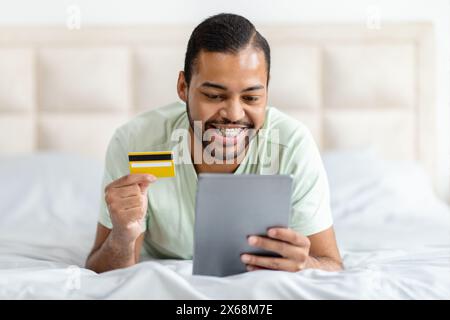 Man Laying on Bed With Credit Card and Tablet Stock Photo
