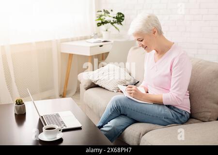 Senior Woman Sitting on Couch, Taking Notes Stock Photo