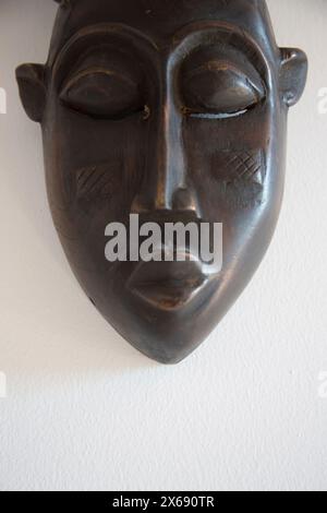 African mask made of dark wood hangs on a white wall Stock Photo