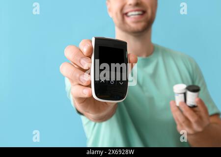 Handsome young happy diabetic man with glucometer and jars of pills on blue background, closeup Stock Photo