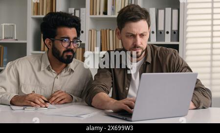 Two diverse anxious displeased businessmen Arabian Indian Caucasian men male colleagues coworkers develop business project online together Stock Photo