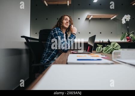 Young curly-haired man in casual wear at office, making a phone call while looking away Stock Photo
