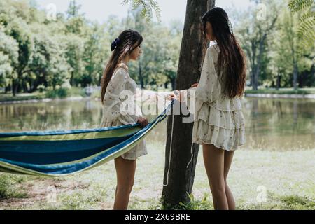 Two friends setting up a hammock by the lakeside in a park on a sunny day Stock Photo