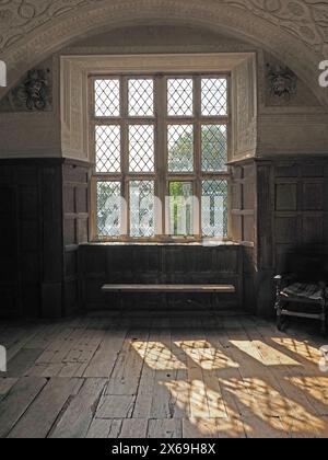 sunlight streaming through recessd ancient mullion window in historic house casting shadows onto timber floor boards Stock Photo