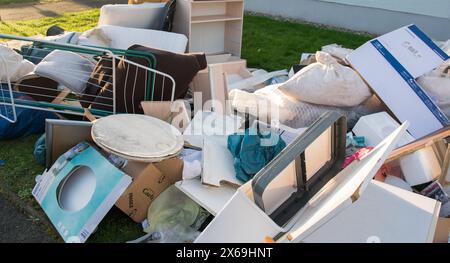 Big garbage with old wood furniture, toys, boxes, plastic bags on a street and green grass in spring sunny trash dump day in Germany. Stock Photo