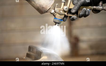Close-up image of a skilled worker's gloved hands using a professional spray gun to paint a car part, highlighting the precision spray and fine mist. Stock Photo