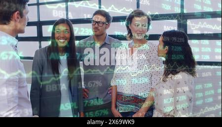 Image of trading board over diverse happy colleague discussing while standing in office Stock Photo