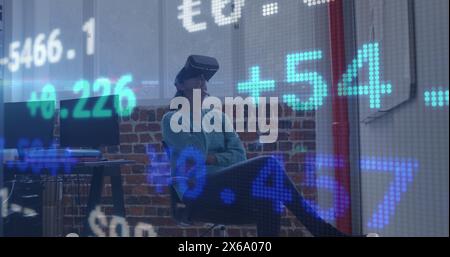 Image of trading board over caucasian woman sitting on chair and using vr headset in office Stock Photo