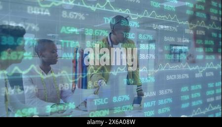 Image of trading board over diverse coworkers discussing reports on laptop in office Stock Photo
