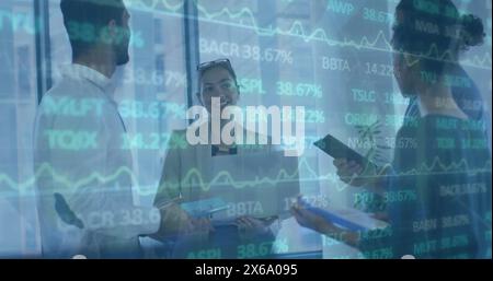 Image of trading board over diverse coworkers standing and discussing in office Stock Photo