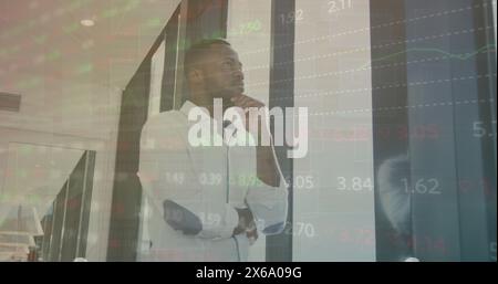 Image of multicolored trading board, thoughtful african american man looking through window Stock Photo