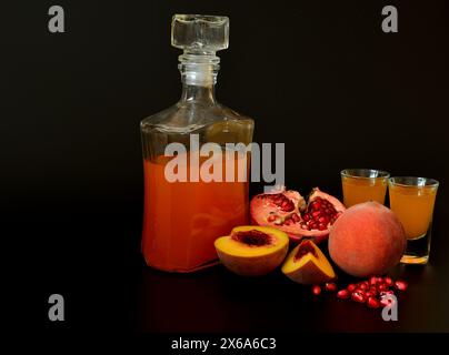 Pomegranate peach liqueur on a black background, a bottle and two glasses with homemade alcohol and ripe fruits. Close-up. Stock Photo