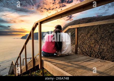married couple sitting together on the stairs and looking at sunset view Stock Photo