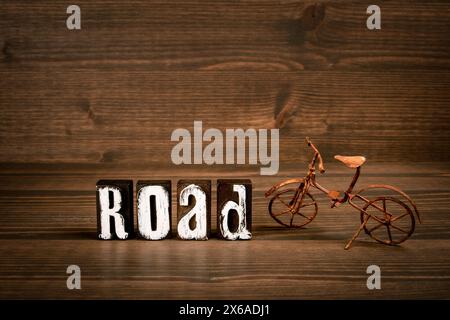 ROAD. Text from alphabet blocks and rusty miniature bicycle on wood texture background. Stock Photo