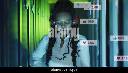 Image of icons and numbers over african american female it technician by computer servers Stock Photo