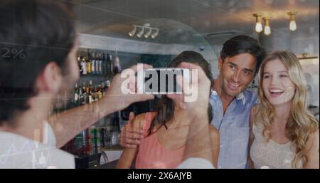 Image of data processing over caucasian male waiter taking picture of group of friends at a bar Stock Photo