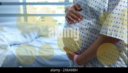 Image of green spots over biracial pregnant woman touching her stomach in hospital Stock Photo