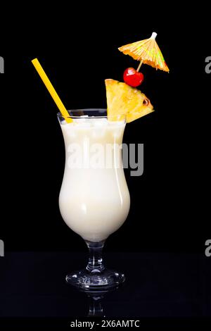 Pina colada drink with straw, slice of pineapple, maraschino cherry and cocktail umbrella isolated on black background. Stock Photo