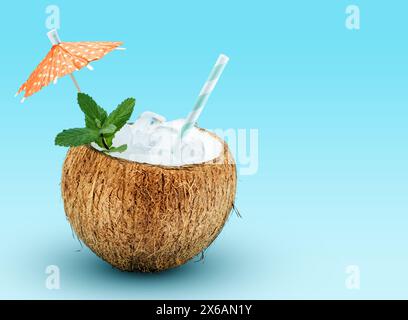 Exotic cocktail served in coco shell garnished with mint, drinking straw and cocktail umbrella pick on blue background with space for text. Stock Photo