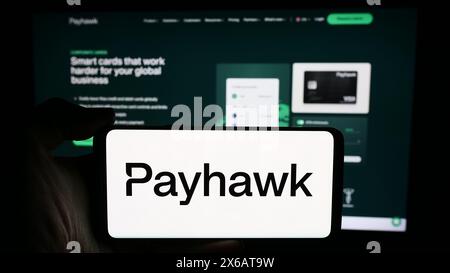 Person holding cellphone with logo of British spend management company Payhawk Limited in front of business webpage. Focus on phone display. Stock Photo