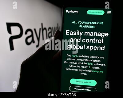 Person holding smartphone with webpage of British spend management company Payhawk Limited in front of logo. Focus on center of phone display. Stock Photo