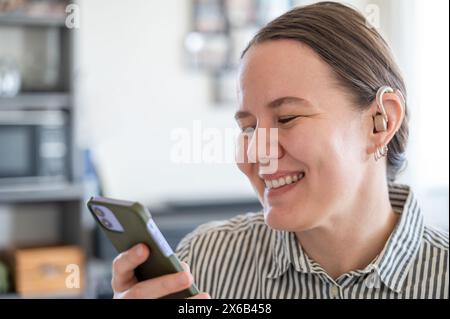 Woman with hearing aid using smartphone and smiling Stock Photo