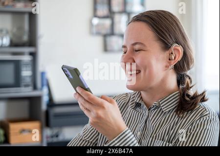 Woman with hearing aid using smartphone and smiling Stock Photo