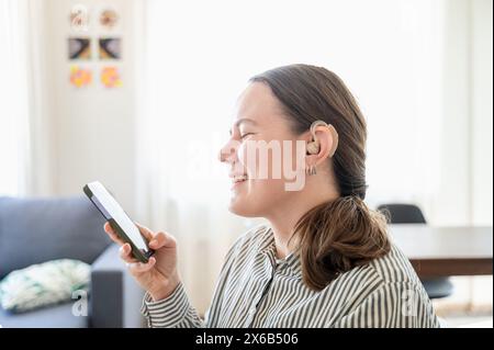 Woman with hearing aid using smartphone and smiling Stock Photo