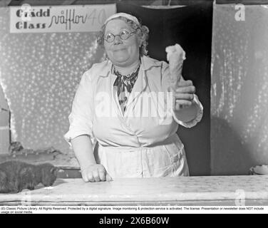 Ice cream in the 1940s. The woman selling ice cream is handing holding cone of vanilla ice cream. A car is seen on the counter, licking on a spot where ice cream is spilled.  14 June 1941. Kristoffersson ref 188-5 Stock Photo