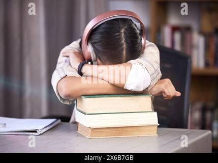 Headphones, books and girl with sleeping in library for studying, burnout and knowledge for exam. University, student and tired with rest on table for Stock Photo
