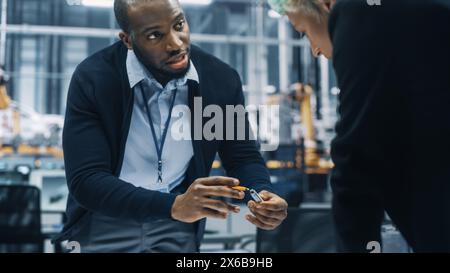 Two Young Automotive Engineers Working in Office at Car Factory. Industrial Designer and Colleague Discussing Different Applications of a Metal Pinion Gear in Personal Mobility Vehicles. Stock Photo