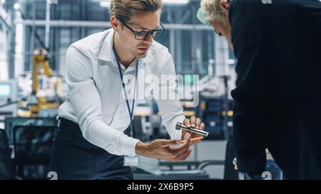 Two Young Automotive Engineers Working in Office at Car Factory. Industrial Designer and Colleague Discussing Different Applications of a Metal Pinion Gear in Personal Mobility Vehicles. Stock Photo