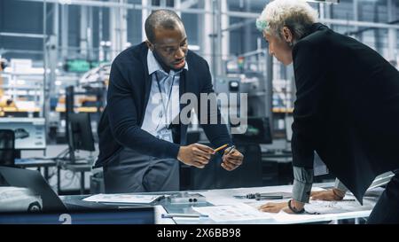 Two Young Automotive Engineers Working in Office at Car Factory. Industrial Designer and Colleague Discussing Different Applications of a Metal Pinion Gear in Personal Mobility Vehicles. Stock Photo