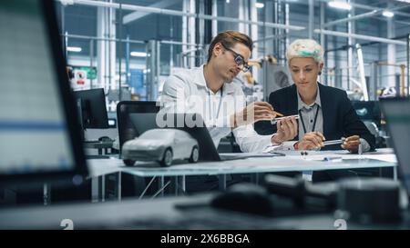 Two Young Automotive Engineers Working in Office at Car Factory. Industrial Designer and Colleague Discussing Different Applications of a Metal Pinion Gear in Personal Mobility Vehicles. Stock Photo