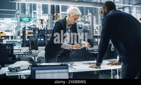 Two Young Automotive Engineers Working in Office at Car Factory. Industrial Designer and Colleague Discussing Different Applications of a Metal Pinion Gear in Personal Mobility Vehicles. Stock Photo