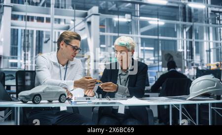 Two Young Automotive Engineers Working in Office at Car Factory. Industrial Designer and Colleague Discussing Different Applications of a Metal Pinion Gear in Personal Mobility Vehicles. Stock Photo