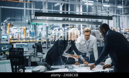 Young Diverse Team of Automotive Engineers Working in Office at Car Factory. Industrial Designer Talks About Electric Engine Parts with Colleagues, Discussing Different Technological Applications. Stock Photo