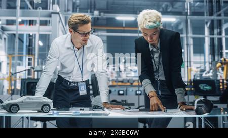 Two Young Automotive Engineers Working in Office at Car Factory. Industrial Designer and Colleague Discussing Different Applications of a Metal Pinion Gear in Personal Mobility Vehicles. Stock Photo