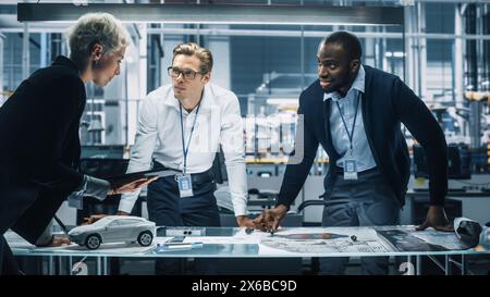 Young Diverse Team of Automotive Engineers Working in Office at Car Factory. Industrial Designer Talks About Electric Engine Parts with Colleagues, Discussing Different Technological Applications. Stock Photo
