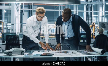 Two Automotive Engineers Working in Office at Car Factory. Industrial Designer Shows Conceptual Electric Engine Parts to Colleague, Discussing Different Applications in Technological Laboratory. Stock Photo
