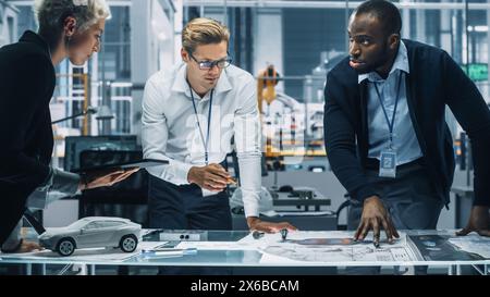 Young Diverse Team of Automotive Engineers Working in Office at Car Factory. Industrial Designer Talks About Electric Engine Parts with Colleagues, Discussing Different Technological Applications. Stock Photo