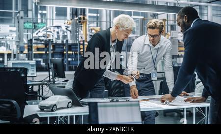 Young Diverse Team of Automotive Engineers Working in Office at Car Factory. Industrial Designer Talks About Electric Engine Parts with Colleagues, Discussing Different Technological Applications. Stock Photo