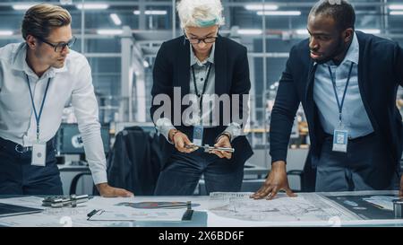 Young Diverse Team of Automotive Engineers Working in Office at Car Factory. Industrial Designer Talks About Electric Engine Parts with Colleagues, Discussing Technical Blueprint for Mobility Project. Stock Photo