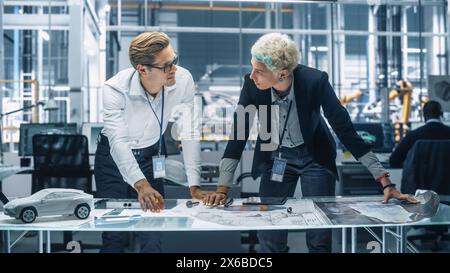 Two Young Automotive Engineers Working in Office at Car Factory. Industrial Designer and Colleague Discussing Different Applications of a Metal Pinion Gear in Personal Mobility Vehicles. Stock Photo