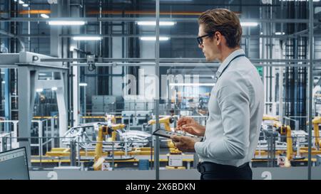 Handsome Engineer in Glasses and White Shirt Using Tablet Computer and Looking Out of the Office at a Car Assembly Plant. Industrial Specialist Working on Vehicle Design in Technological Facility. Stock Photo